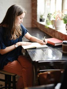 A woman conducting a mental health assessment. She's writing in a notebook in front of a window.